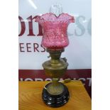 A Victorian brass oil lamp, with a cranberry glass shade