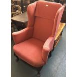A wingback armchair with scrolling arms, upholstered in red, on carved cabriole legs