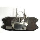 A Swedish metal sculpture of a trawler affixed to a piece of driftwood, titled 'Trålare', signed