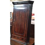 A George III oak hanging corner cupboard, dentil cornice above cupboard door opening to three shaped