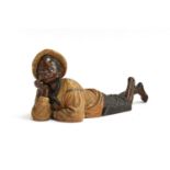 An early 20th century figurine of a recumbent boy wearing a tam o'shanter, marks to base, 9.5cm high