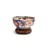 An Imari bowl with scalloped edges and hand painted interior and surround detail, on carved hardwood