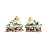A pair of famille verte biscuit porcelain Budai figures, with green underglaze robes, reclined