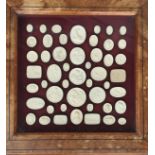 A small 19th century oak display table containing a collection of 49 intaglio seals, 59cm square,