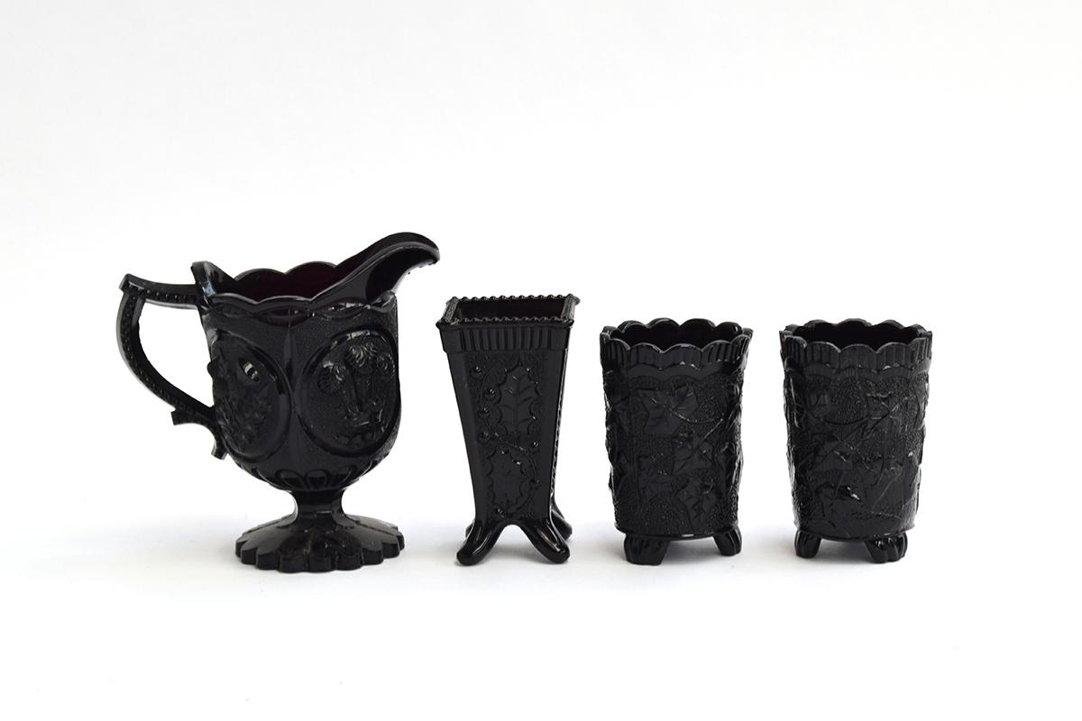 Four pieces of Victorian black pressed glass, to include a four-sided vase, the panels decorated