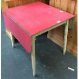 A 1950s white painted kitchen table with red formica drop leaf top, 76cmH