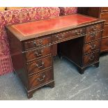 A kneehole desk, with tooled red leather skiver, above the traditional arrangement of drawers, on