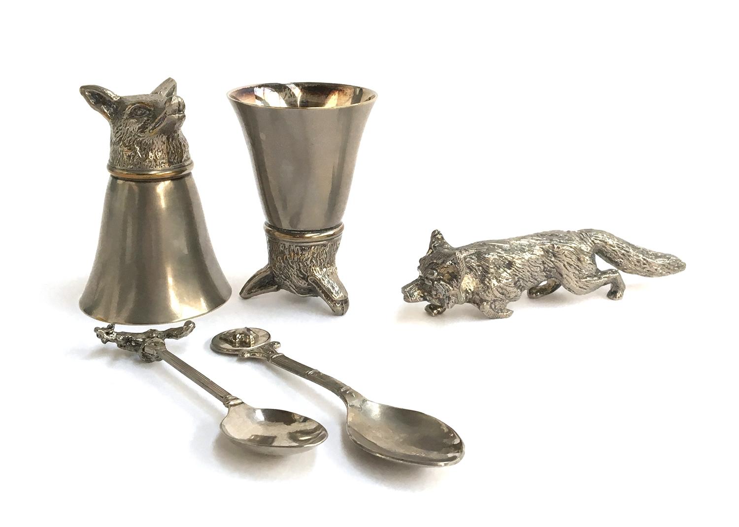 A pair of fox mask stirrup cups, each approximately 8cm high; together with two teaspoons, one
