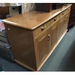 A blond oak mid-century sideboard, comprising four drawers over two sliding cupboard doors,