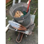 A galvanised wheelbarrow with dustbin lid, planter and wicker basket