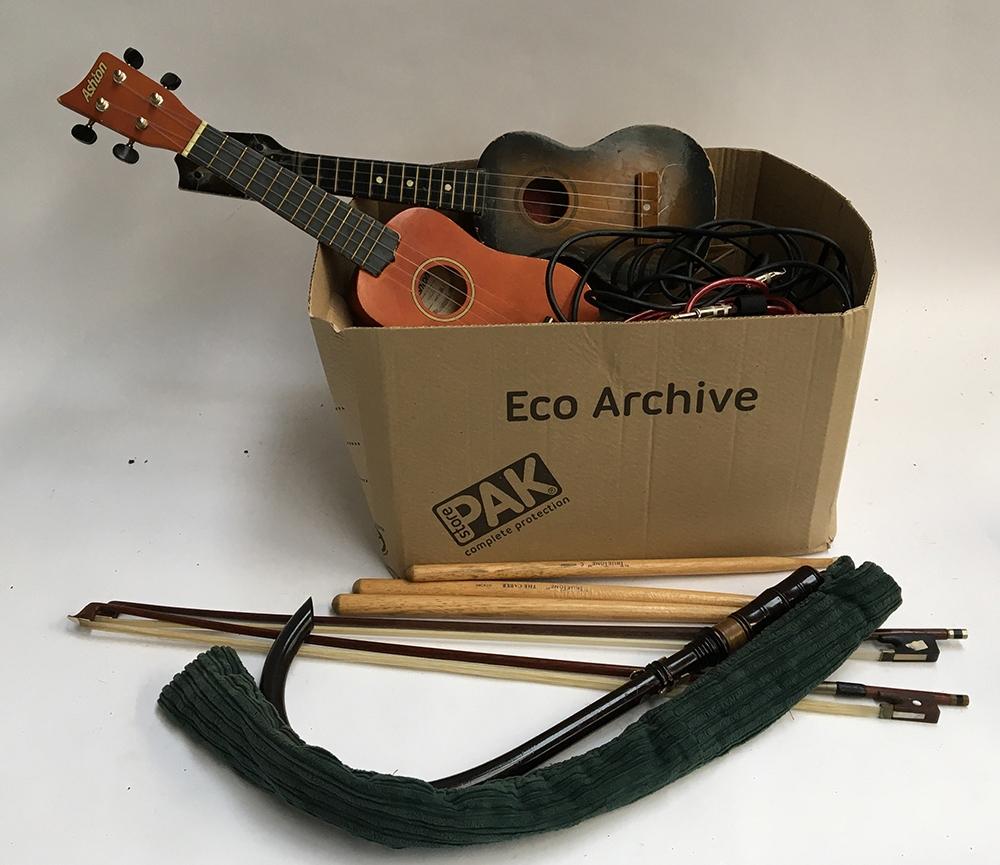 A mixed box of musical instrument accessories, mostly strings, two ukuleles; practice pipes;