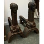 A very unusual pair of heavy cast iron firedogs, each with stylised face over lion passan, 49cmH