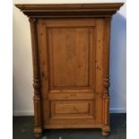 A pine cupboard, boarded pediment top over single cupboard door flanked by corinthian columns, on