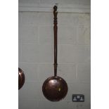 A copper warming pan with turned wooden handle
