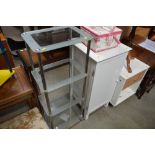 A white painted single drawer cabinet with a four tier glass shelving unit