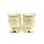 A pair of Belleek urns, decorated with cherubs in the sea, raised on scroll and shell bases, 27cm