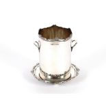 A George V silver bottle stand, having ribbon tied shaped borders and raised on bun feet, 17.5cm