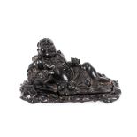 An Oriental carved hardwood figure of a reclining Joss man, with dragon, 39cm long