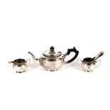 A three piece Indian white metal tea set, with stylised decoration, the teapot having wooden
