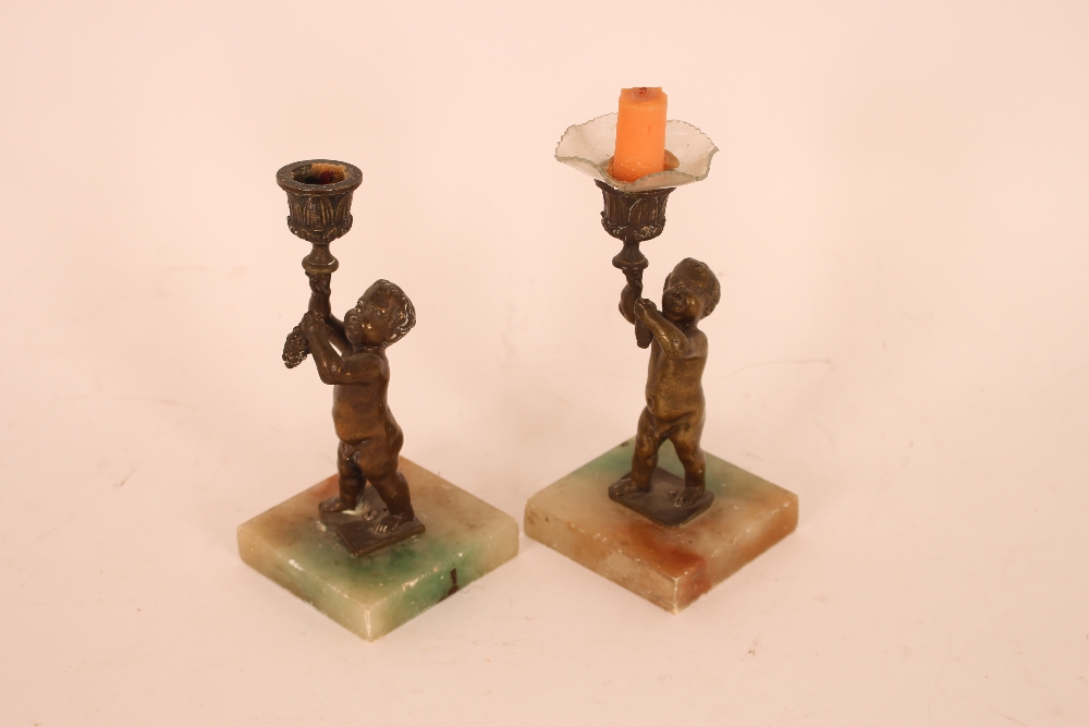 A pair of bronzed cherub candlesticks, raised on s