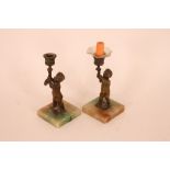 A pair of bronzed cherub candlesticks, raised on s