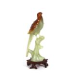 A jade figure of a bird, seated on a branch, raised on a carved hardwood stand, 23cm high