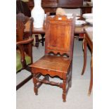 An antique oak hall chair, having shaped back, solid panel and seat, raised on turned block