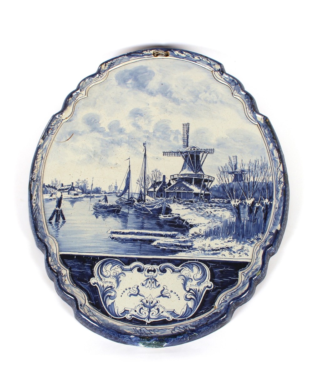 A Delft plaque, depicting winter canal scene with barges and windmills, of cartouche shape, 60cm x