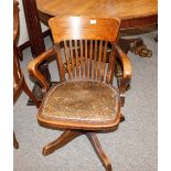 An early 20th Century oak revolving desk chair, having rail back, upholstered seat on quatrefoil