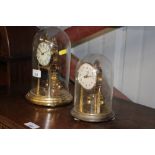 Two brass anniversary clocks, under glass domes