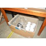 A box containing various mugs, glassware, and a ca