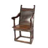 An antique oak wainscot chair, having carved foliate decoration, panelled back, swept arms above