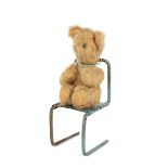 A miniature Teddy Bear, seated on a metalwork chair, 9cm high