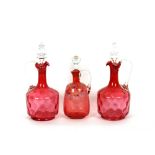 A pair of cranberry dimpled glass claret jugs, having clear glass handles and stoppers; and