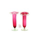 A pair of cranberry spill vases, having crimped fold over rims and clear glass bases, 19cm high