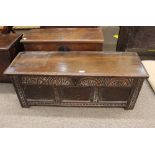 An antique carved oak coffer, having candle box interior and triple panel carved front, iron strap