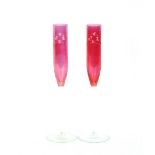 A pair of cranberry glass flutes, with etched foliate decoration on clear glass stems and bases,