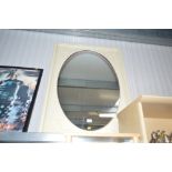 A large oval wall mirror contained in cream painte