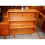 A teak open fronted bookcase, raised on rounded ta