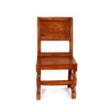 An antique oak hall chair, having carved panel back and solid seat, raised on turned block