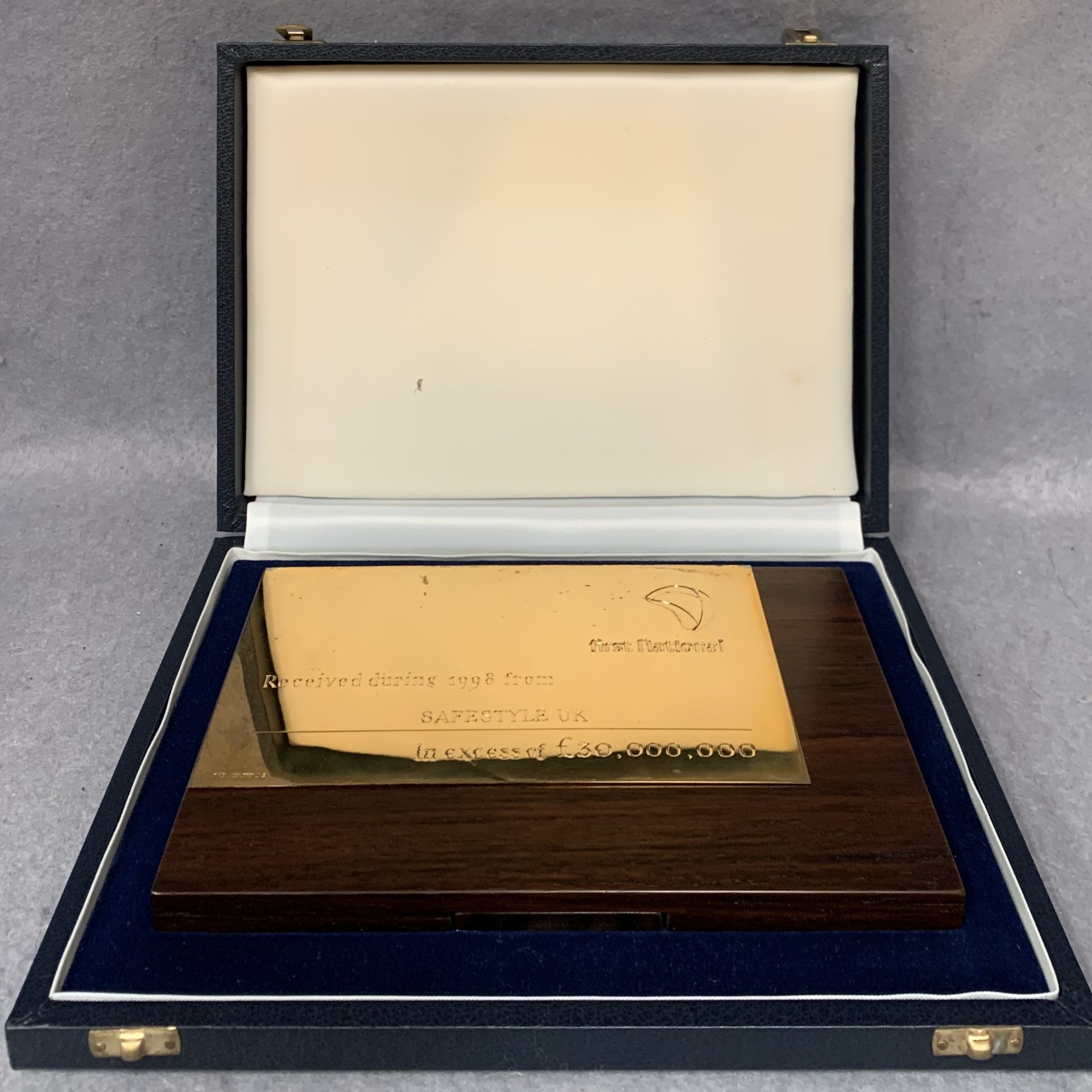 A silver presentation plaque from The First National Bank mounted on a walnut finish frame complete