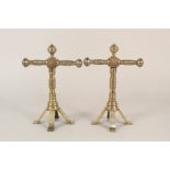 A pair of aesthetic movement brass fire dogs with turned tool rests and columns and four splayed