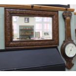 A carved oak wall mirror with bevelled glass plus a carved oak aneroid barometer (as found)