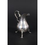 A silver cream jug with wavy rim on three legs,