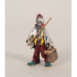A silver enamel decorated clown with fishing bag and rod