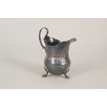 A Georgian silver cream jug with engraved floral decoration on three paw feet,