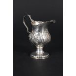 A silver cream jug with embossed floral decoration on pedestal base,