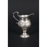 An 18th Century silver cream jug with embossed decoration on pedestal base (marks are rubbed)