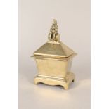 A sarcophagus shaped brass tobacco jar and cover having finial in the form of a man sitting on a