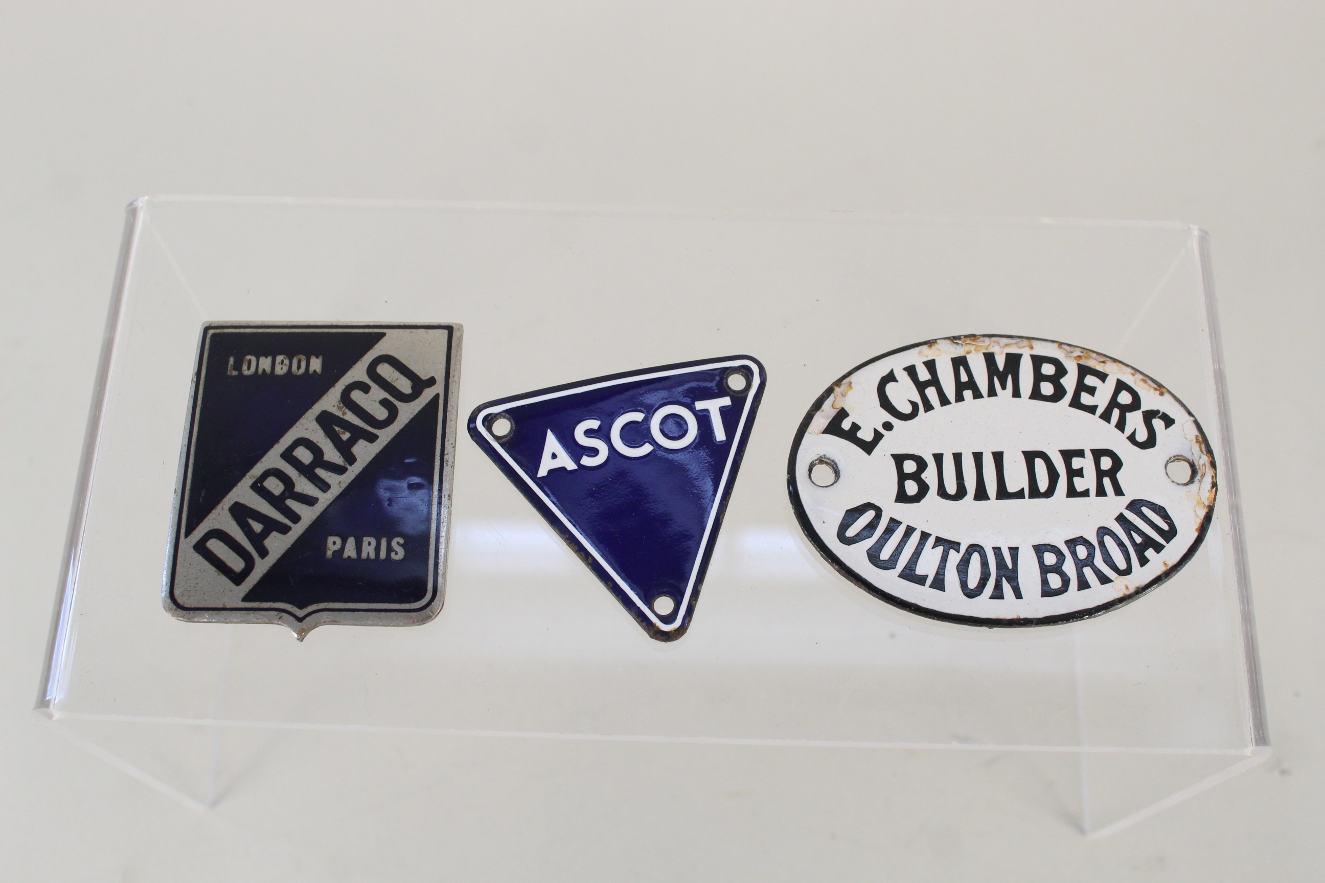 Three enamel badges including 'Darracq' and 'Ascot'